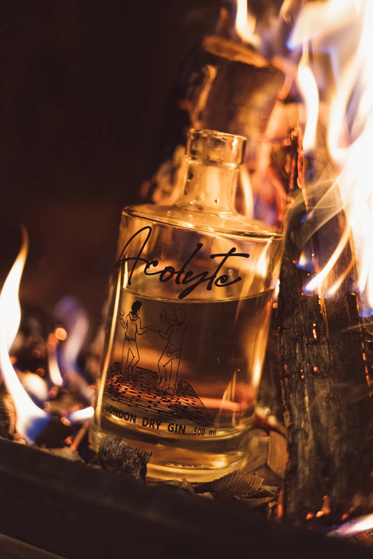 Bouteille de Gin Acolyte devant un feu, permettant de la mettre en valeur et de montrer la pureté de la boisson dans une ambiance réconfortante.